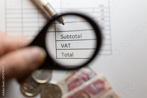 Magnifying glass hold over VAT word. UAE dirhams banknotes and coins on a invoice with VAT box. UAE will implement VAT at the rate of 5% on 1 January 2018.
