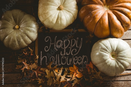 Happy Halloween text on slate by pumpkins amidst autumn leaves