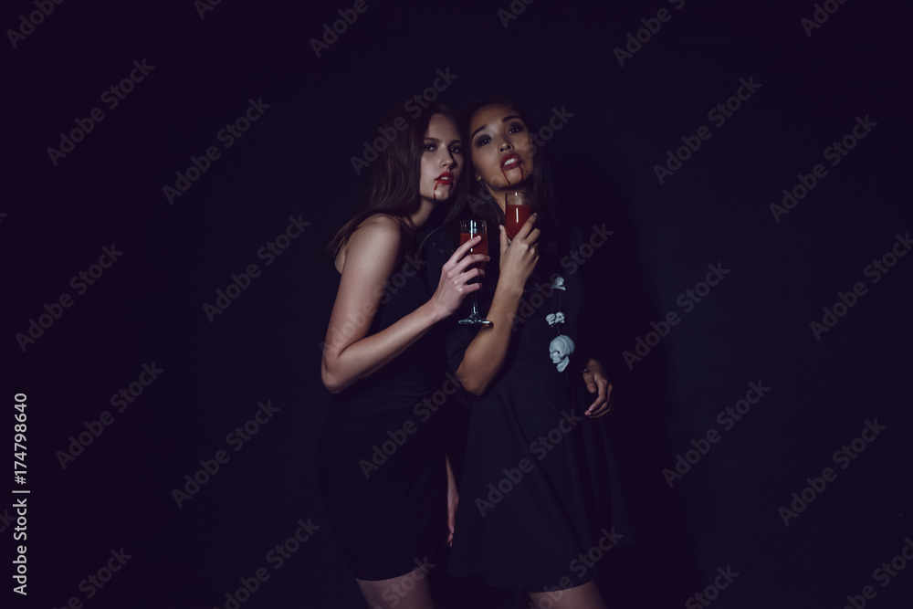 Attractive girls in the image of vampires hold glasses with blood. Halloween. Attractive girls in the image of vampires hold glasses with blood. Halloween.