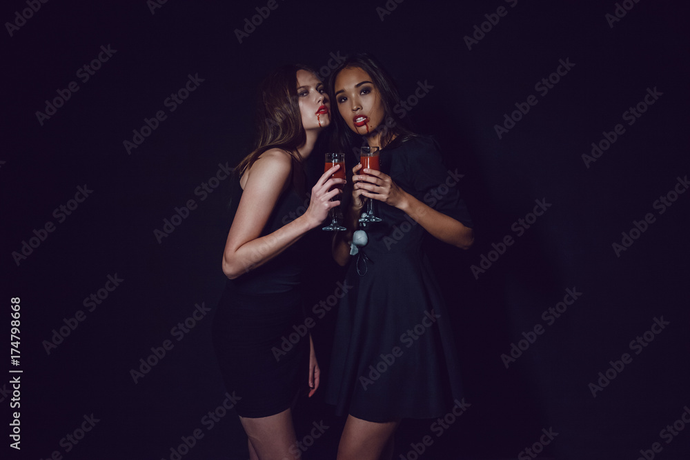 Attractive girls in the image of vampires hold glasses with blood. Halloween. Attractive girls in the image of vampires hold glasses with blood. Halloween.