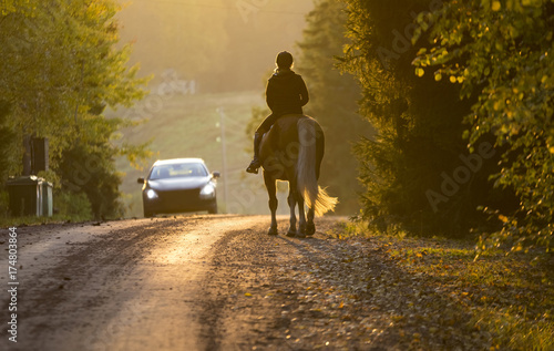 Woman horseback riding on the road in the sunset