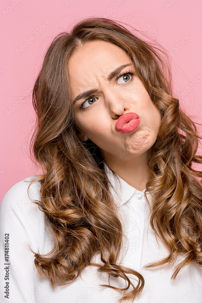 Close-up portrait of a woman doing a fish mouth expression, over a pink background