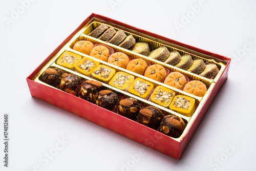 stock photo of Indian sweet or mithai and oil lamp or diya with gift box and flowers on decorative or colourful background, selective focus