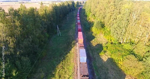 AERIAL railway: Long cargo train transporting wagons across the autumn forest and fields