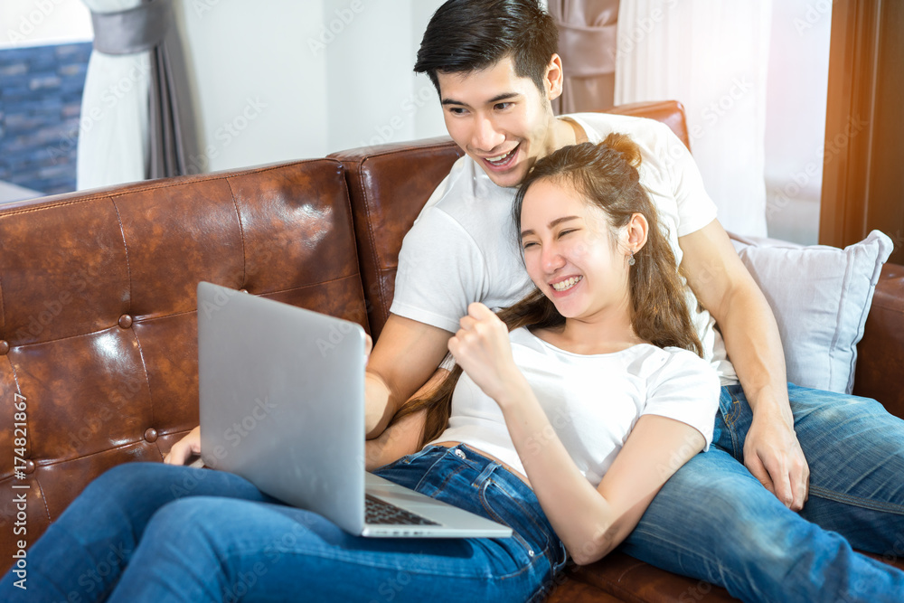 Young couple together man and woman looking laptop computer happy and smile relaxing on sofa in living room at home in holidays weekend