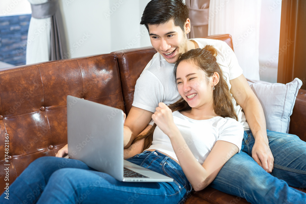 Young couple together man and woman looking laptop computer happy and smile relaxing on sofa in living room at home in holidays weekend Young couple together man and woman looking laptop computer happy and smile relaxing on sofa in living room at home in holidays weekend