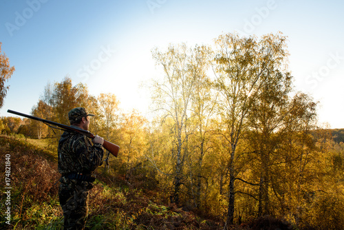 A hunter with a gun in the forest at dawn.
 photo
