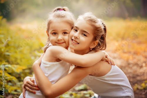 Childhood, family, friendship and people concept - two happy kids sisters hugging outdoors. photo