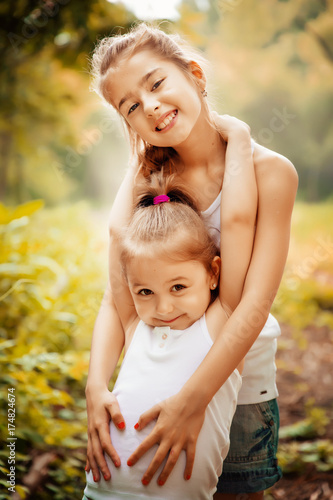 Childhood, family, friendship and people concept - two happy kids sisters hugging outdoors.