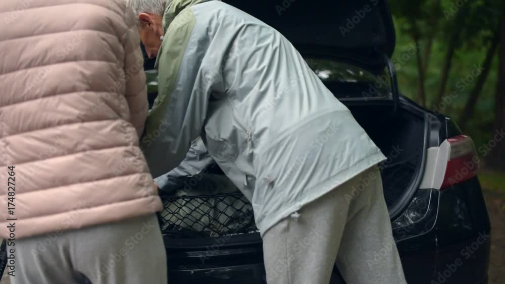Pleasant aged couple packing tourism equipment in the car boot Pleasant aged couple packing tourism equipment in the car boot
