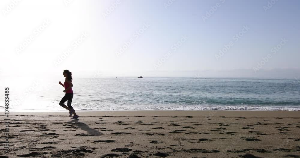 4k video. Adult woman with red shirt and black leggings, or knee pants, running on the beach, side to side, in Benalmadena, Malaga, Andalusia, Spain
