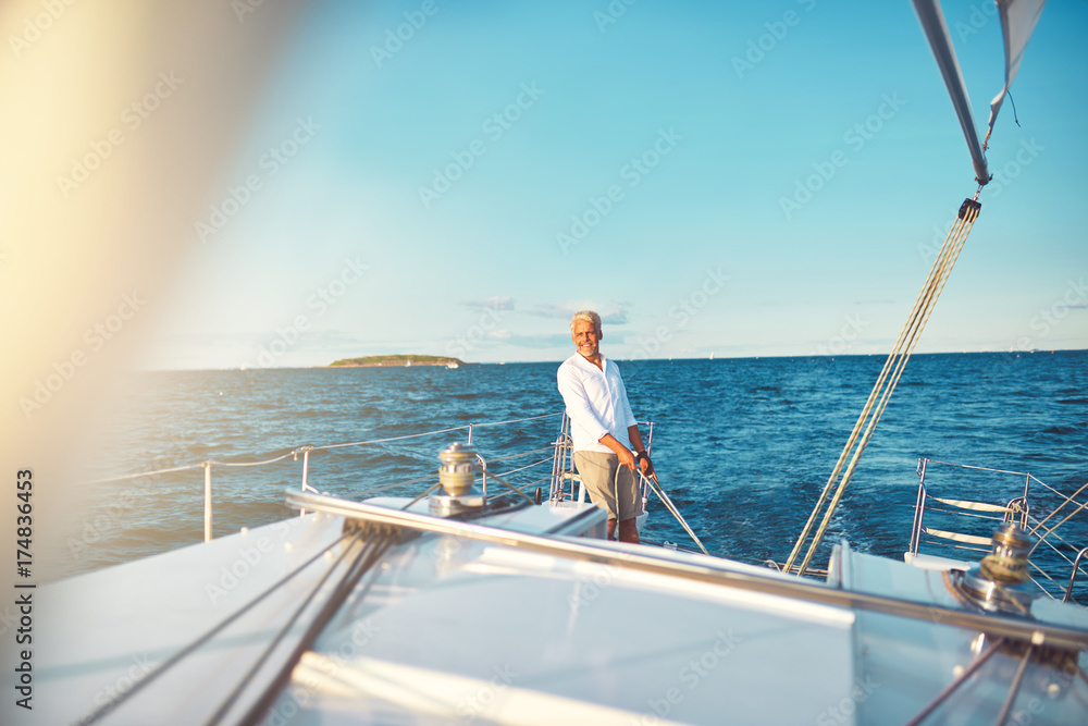 Mature man steering his sailboat on the open ocean Mature man steering his sailboat on the open ocean