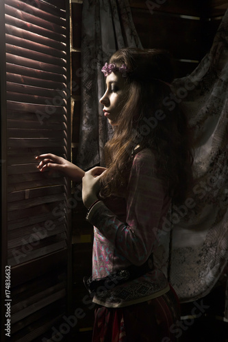 beauty hippie boho woman looks through a shuttered window on a dark background photo