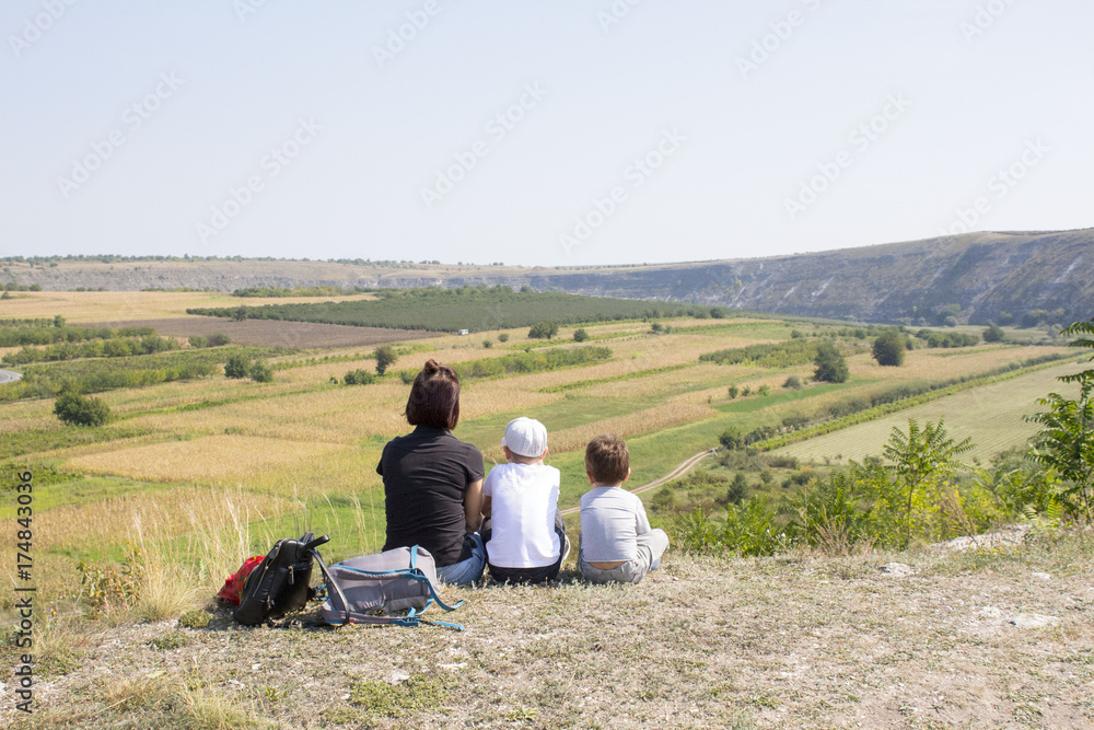 Family in the mountains. mom and two sons  putting backpacks sit on the hill over the mountain. Back view. Concept of travel. summer scene. copy space.