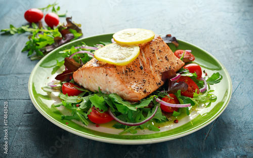 Baked salmon steak with tomato, onion, mix of green leaves salad in a plate. healthy food