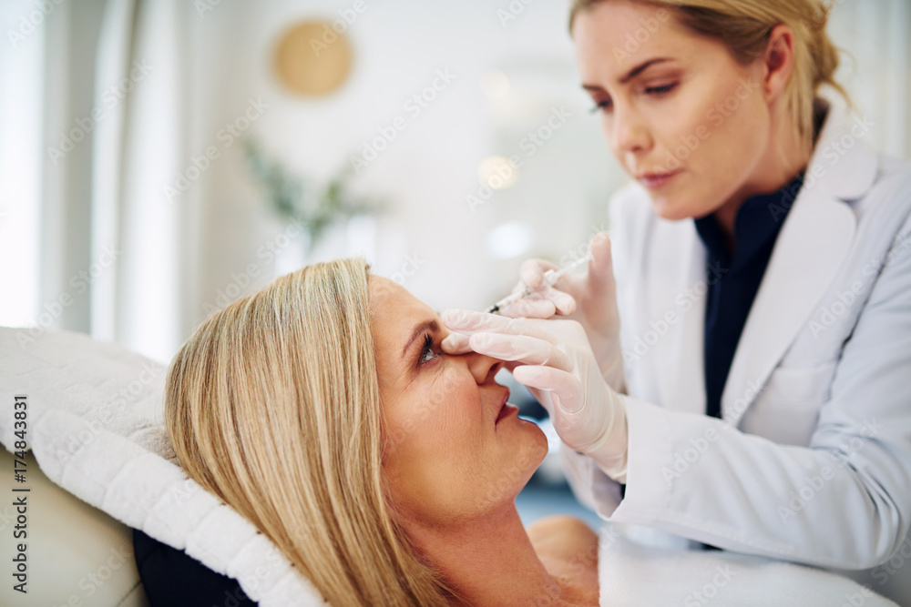 Doctor injecting botox into a mature woman's forehead Doctor injecting botox into a mature woman's forehead