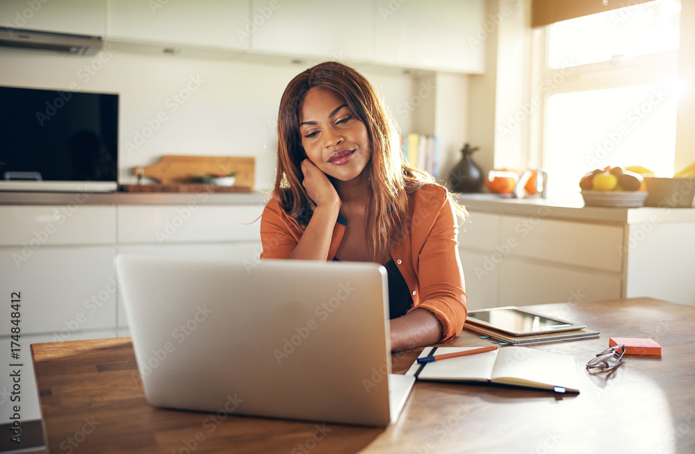 Smiling female entrepreneur working on a laptop in her kitchen Smiling female entrepreneur working on a laptop in her kitchen