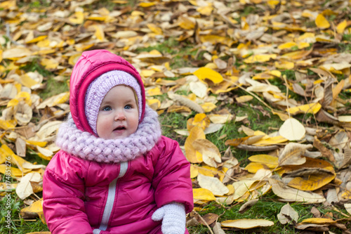 Toddler have fun outdoor in autumn yellow park. Funny baby is sitting in a pile of leaves