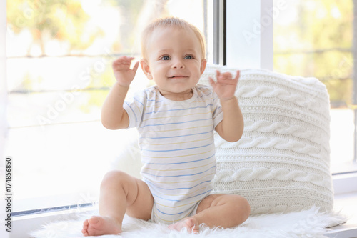 Cute little baby sitting on window sill at home