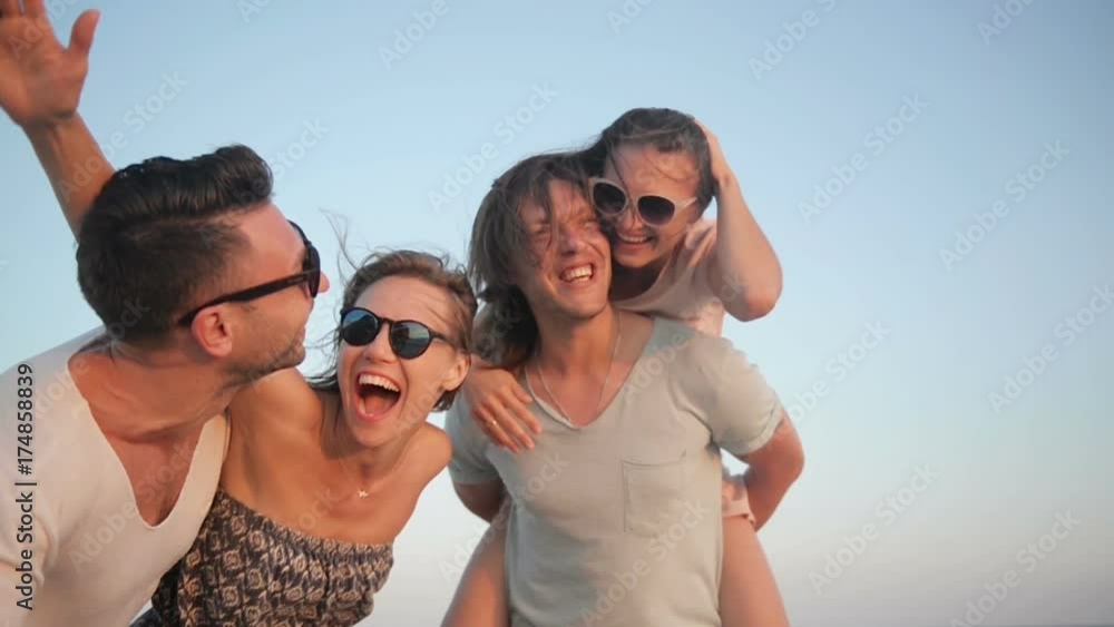 Outdoors Portrait of Happy Young Group of Friends Enjoying Beach Holiday. Two Couples Laughing near the Sea During Summer Time. Outdoors Portrait of Happy Young Group of Friends Enjoying Beach Holiday. Two Couples Laughing near the Sea During Summer Time.
