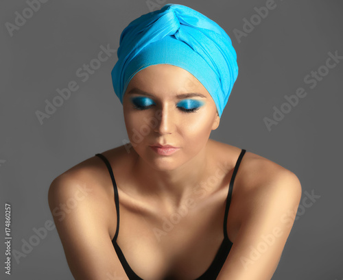 Beautiful young woman in blue kerchief against grey background
