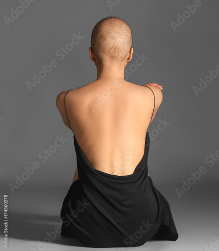 Fotografía Beautiful bald woman in black dress sitting against grey background
