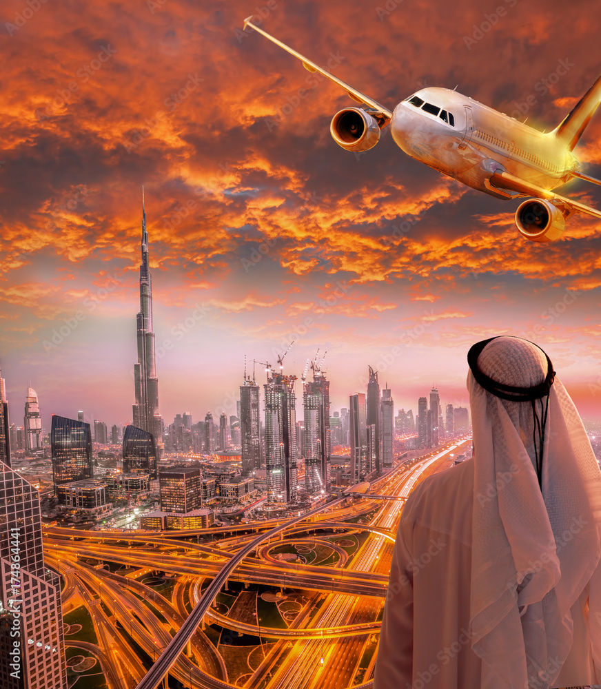 Fototapeta premium Arabski mężczyzna z samolotem lecącym nad Dubajem przed kolorowy zachód słońca w Zjednoczonych Emiratach Arabskich