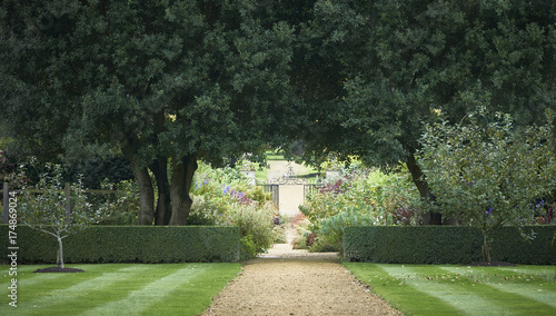 Pathway to an ornate wrought iron gate through landscaped gardens