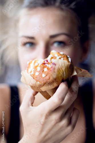 A homemade raspberry cupcake with sugar dots on top in the hand of a blue eyed girl