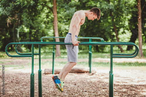 Young fit man doing push ups on bars in an outdoors gym