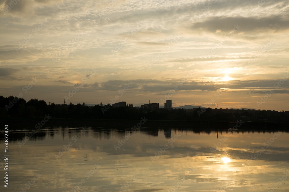 Colorful sunset on the lake with reflections of hills, trees and buildings. Slovakia