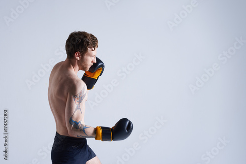 Hardworking young unshaven young European boxer exercising in studio, challening himself, having concentrated look, focused on boxing technique to improve efficiency, preparing for boxing match photo