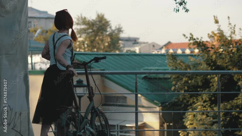 Young redhaired woman riding bicycle in city. Woman with mobile phone Young redhaired woman riding bicycle in city. Woman with mobile phone