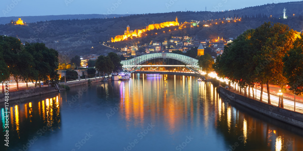 Panorama of night Old Town with Narikala Fortress and illuminated Bridge of Peace across Kura river, Tbilisi, Georgia