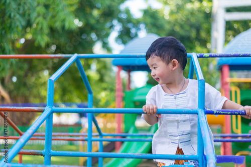 Asian boy hang the metal bar at outdoor playground. © pookpiik