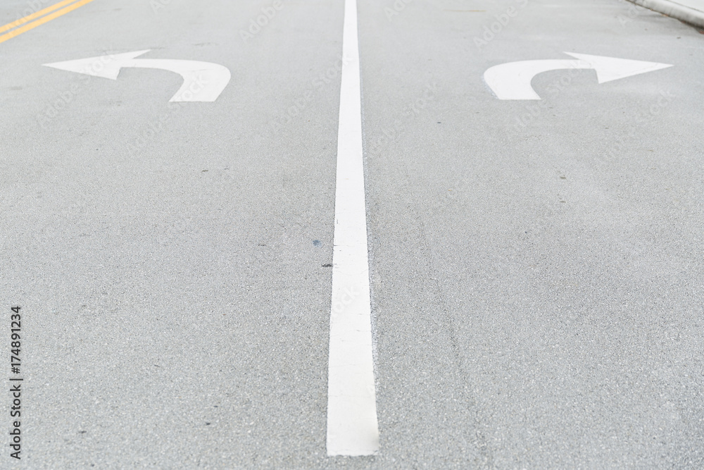 White arrow signs painted on road as direction restriction. Arrow signs as road markings on a street with two lanes