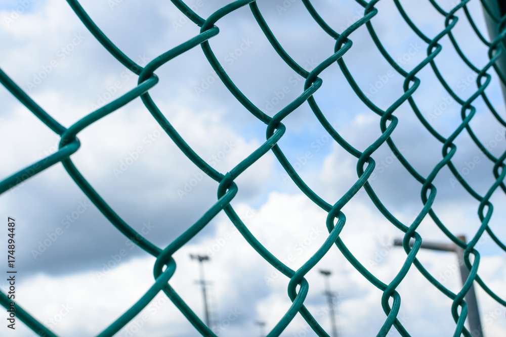 Green metal wire fence under fluffy white clouds and blue sky background. Green metal wire fence under fluffy white clouds and blue sky background.