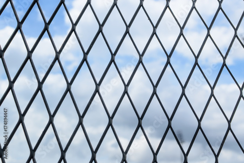 Black solid metallic mesh fence closeup with sky in the background.