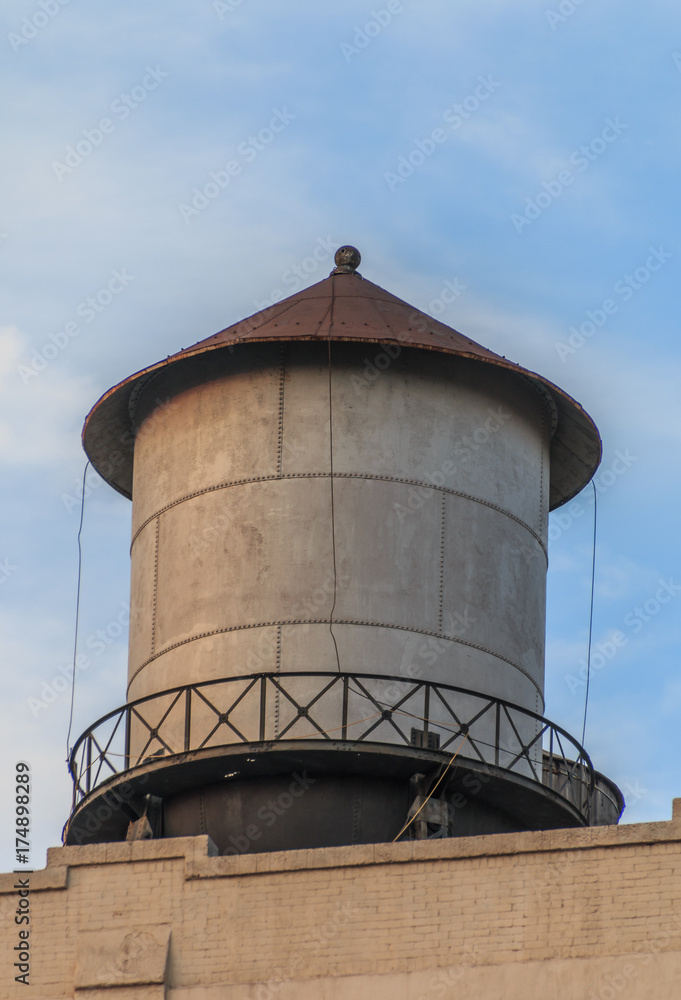 Metal water tank sitting on top of a building. The water tank has a peaked reddish brown roof. It has a metal walkway around it. Metal water tank sitting on top of a building. The water tank has a peaked reddish brown roof. It has a metal walkway around it.