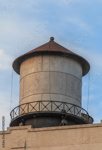 Metal water tank sitting on top of a building. The water tank has a peaked reddish brown roof. It has a metal walkway around it.
