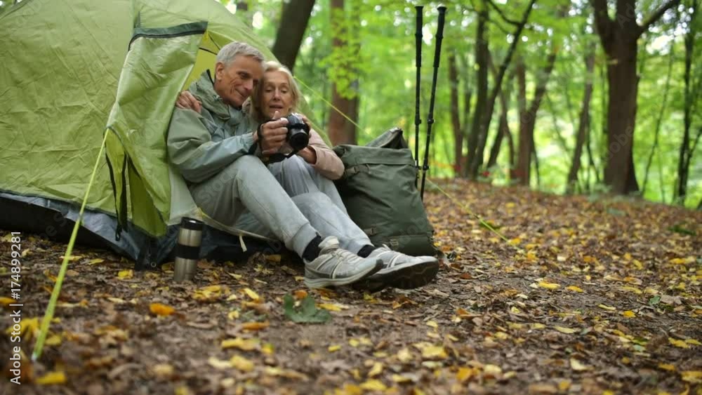 Positive aged couple using photo camera while in the forest Positive aged couple using photo camera while in the forest