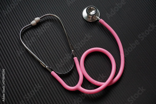 Pink stethoscope on black exercise mat.