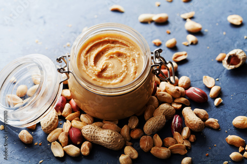 Peanut butter jar and heap of nuts on dark rustic background. photo