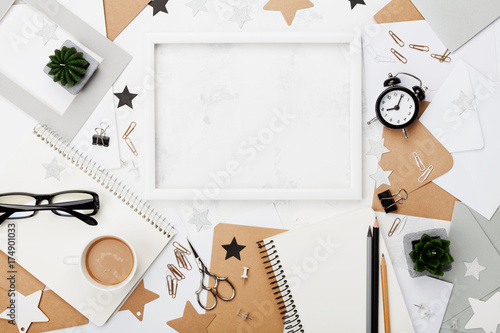 Stylish workplace background. Frame, coffee, office supply, alarm clock and notebook on white desk top view. Flat lay. Copy space for text. Fashion mockup for blogging.