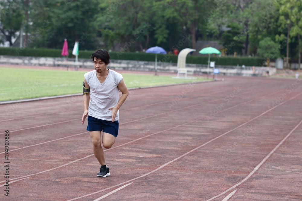 Handsome athlete Asian man running on racetrack in stadium with copy space background. Healthy active lifestyle concept.