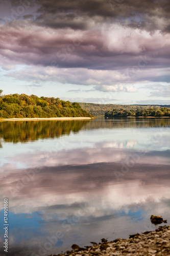 A beautiful autumn landscape, a forest reflected in a river, the sky with clouds.