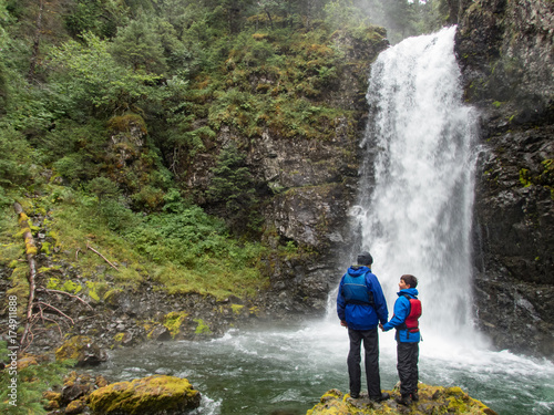 Father and 10 year old son holding hands and discovering remote waterfall near Seward, Alaska photo
