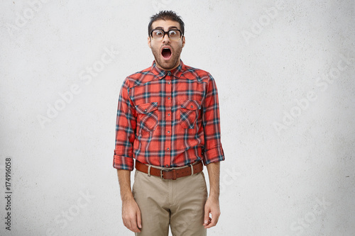 Fotografie Astonished young manager with brunette hair and beard staring at camera in shock