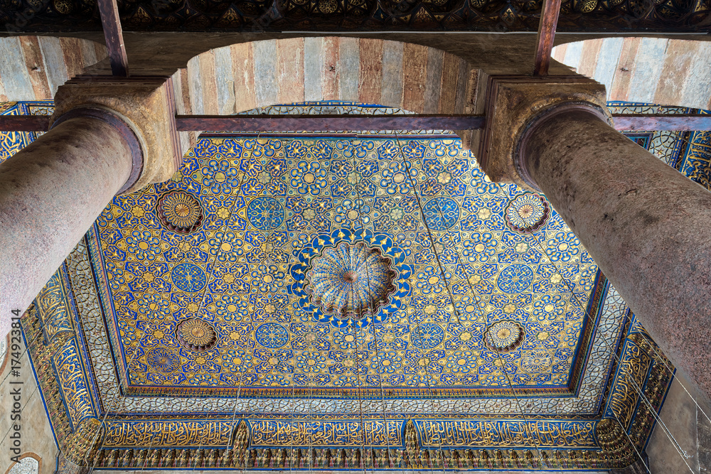 Ornate ceiling with blue and golden floral pattern decorations frammed throught huge arch and two columns at Sultan Barquq mosque, Al Moez Street, Cairo, Egypt