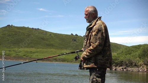 A man with a spinning catches fish in a lake against green mountain. Kuril Islands, Okhotsk Sea
